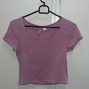 Ljuslila croppad topp från H&M Divided - Enkel och snygg ljuslila croppad topp från H&M Divided. Modellen har korta ärmar, rundad djup urringning och är tillverkad i mjuk bomull. Perfekt att matcha med jeans eller kjol för en chill look.