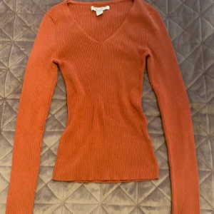 Rosa ribbad tröja från Amisu, Xs  - Ser orange ut I bilden men är Rosa Kolla skära bild Säljer en snygg Rosa ribbad tröja från Amisu i storlek XS. Tröjan har v-ringad hals, långärmade smala ärmar och är figurnära i passformen. Perfekt för dig som gillar stilrena och enkla plagg med lite edge. Materialet är mjukt och stretchigt stickat.