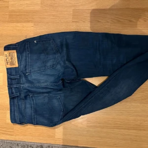 Replay Anbass jeans blå, stl 31/30 - Säljer ett par snygga Replay Anbass jeans i mörkblå. Klassisk  med raka ben och diskreta slitningar. Jeansen har en skön stretch och har detaljerade sömmar på bakfickorna.