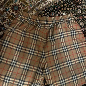 Rutig Burberry shorts XL - Äkta Burberry shorts i klassiskt beige rutigt mönster med röda och svarta linjer. Elastiskt band på midja och funkar till både vad och vindshorts. Xl men passar också L pris kan alltid diskuteras 