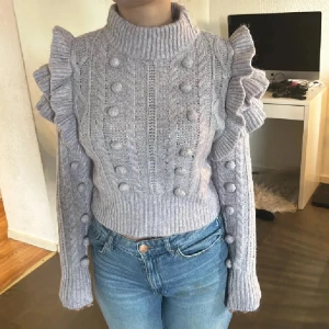 Lila stickad volangtröja med polokrage - Superfin lila stickad tröja med polokrage och volangdetaljer på axlarna. Tröjan har ett coolt flätmönster och bollar längs ärmar och framstycke. Croppad modell med långa ärmar och ribbade muddar. Perfekt för dig som vill sticka ut lite extra! Använd gärna köp nu❤️