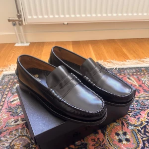 Sebago, Slip-ins black - Nypris 3200kr. Klassiska svarta loafers från Sebago i blankt skinn. Snygg penny loafer-design med rund tå och diskreta sömmar runt tån. Perfekta för en clean och tidlös look, passar till både jeans och kostym. Skorna har platt sula och är riktigt bekväma att bära. 