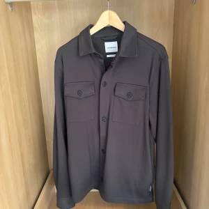 Mörkbrun overshirt från Lindbergh - Stilren mörkgrå overshirt från Lindbergh. Perfekt för hösten. Och som har aldrig använts.