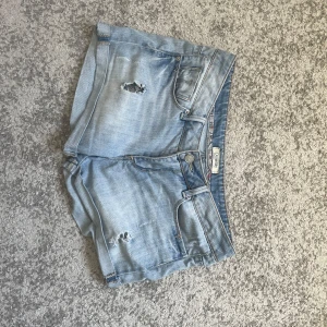 Ljusblå jeansshorts från Denim Life - Snygga ljusblå jeansshorts från Denim Life by Pimkie med slitna detaljer och klassisk femficksdesign. Shortsen har låg midja, knapp och dragkedja framtill samt bälteshällor. Perfekta för sommarens chill dagar.