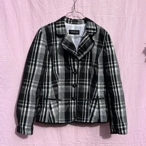 Rutig svartvit kavaj från Betty Barclay - Snygg kavaj från Betty Barclay i svartvitt rutigt mönster. Klassisk krage, knäppning framtill med tre knappar och figursydd passform. Perfekt för dig som vill sticka ut med en stilren och trendig look.