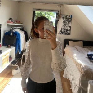 Vit polotröja med spetsärmar - Superfin vit polotröja med ribbad kropp och långa, puffiga spetsärmar. Tröjan har en hög hals och är figurnära i modellen. Perfekt för dig som vill ha något stilrent men ändå med en twist. 