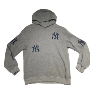 Grå New York Yankees hoodie - Säljer en grå hoodie med mörkblå New York Yankees-loggor på bröstet, magen och båda ärmarna. Tröjan har huva och långa ärmar, perfekt för dig som gillar sportig streetstyle. Mjuk bomullskänsla och klassisk passform. Skirv för funderingar. 