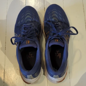 Blå Asics GT-2000 11 sneakers - Säljer ett par Asics GT-2000 11 sneakers i marinblått med orange detaljer och logga på sidan. Skorna har snörning, platt sula och är tillverkade i syntetmaterial med mesh-överdel för bra ventilation. Perfekta för träning och löpning, riktigt sköna och snygga på foten.