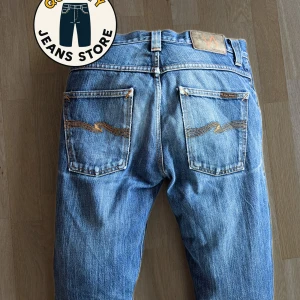 Nudie Jeans grim tim - Snygga blå jeans från Nudie Jeans i modellen Grim Tim. Jeansen har klassisk femficksdesign, orangea sömmar och slim passform. Tillverkade i 100% ekologisk bomull för en skön känsla och schysst stil. Perfekta för dig som gillar en tidlös look.