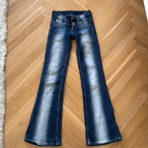 Blå bootcut jeans från Ship Monday/weekday - Säljer ett par blå bootcut jeans med snygga slitningar och ljusa partier framtill och baktill. Jeansen har klassisk femficksmodell, låg midja och dragkedja. Perfekta för dig som gillar en retro vibe och vill ha ett par jeans med riktigt schysst passform. kostar nya 400