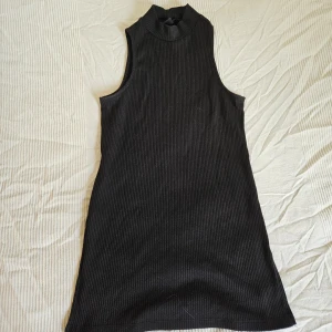 Lång ribbad ärmlös faux-turtleneck - Låång ärmlös top med mock neck/faux turtleneck, Steve Jobs vibes, ribbat svart tyg. Slitsar vid sidorna som en cool detalj, gör den också lättare att stoppa in i ett par byxor. 