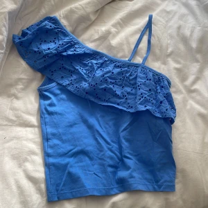 Blå oneshoulder topp från MNG - Snygg blå oneshoulder topp från MNG med volang och broderade blommor längs axeln. Använt en gång köpt för två hundra köpt i Italien.