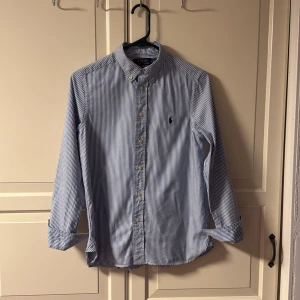 Polo Ralph Lauren skjorta - Tja! Säljer en sjukt snygg blå och vit randig Polo Ralph lauren skjorta som passar perfekt nu inför sommaren. Perfekt till både vardag och fest. Skick: 9/10 använd 3-4 gånger fof fint skick inga defekter. Storlek: 16 passar runt 155-165 modellen i bilden är 165cm. Pris: 649kr köpt för nypris på kidsbrandstore för 1099kr. Pris kan diskuteras vid snabb affär💨. Kom DM vid fler bilder eller funderingar🥰