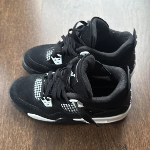 Svarta Nike Air Jordan 4 sneakers - Snygga svarta Nike Air Jordan 4 sneakers med vita detaljer och klassisk Jumpman-logga på hälen. Skorna har snörning, meshpaneler och en robust sula. Ovandelen är i mocka och textil, vilket ger en cool och sportig vibe. Perfekta för dig som gillar streetstyle. Låda tillkommer. Pris kan diskuteras 