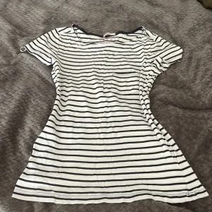 Randig t-shirt från Esprit - Vit och svart randig t-shirt från Esprit med rund halsringning och kort ärm. Toppen har en liten bröstficka på vänster sida och är gjord i mjuk bomull. Perfekt för en chill och avslappnad stil.