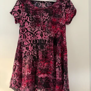 Mönstrad kortklänning  - Kortklänning i ett coolt rosa och svart mönster. Klänningen har rund hals, korta ärmar och är tillverkad i mjuk polyester. Den har en avslappnad passform och ett unikt, nästan abstrakt mönster som verkligen sticker ut.