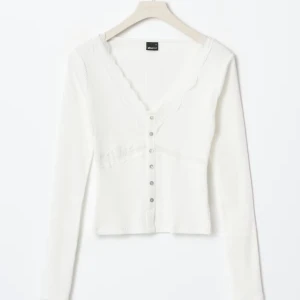 Vit ribbad topp med knappar Gina Tricot - Superfin vit ribbad topp från Gina Tricot med v-ringning och långa ärmar. Toppen har dekorativa knappar framtill och en croppad passform som ger en trendig look. Perfekt att styla med jeans eller kjol för en fräsch outfit.