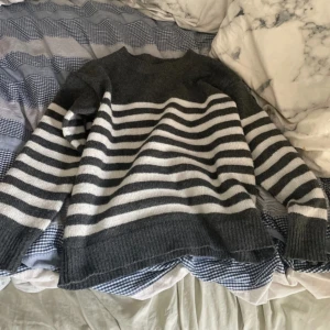 Randig stickad tröja i grått och vitt - Mysig stickad tröja med breda grå och vita ränder. Tröjan har rund halsringning, långa ärmar och ribbade muddar vid ärmslut och nederkant. Perfekt för lager-på-lager och chill dagar.