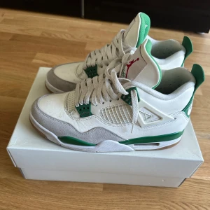 Nike SB Air Jordan 4 Pine Green - Nike SB Air Jordan 4 Pine Green sneakers med vit och grå ovandel i skinn och mocka, gröna detaljer och klassisk Jumpman-logga på plösen. Snygg retrostil med meshpaneler, snörning och gummisula. Använd fåtal gånger. Säljer då de är för små för mig.