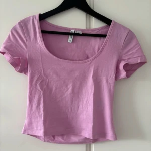 Ljusrosa croppad topp från H&M - Säljer en ljusrosa croppad topp från H&M Basic. Toppen har korta ärmar, rundad djup urringning och är tillverkad i mjuk bomull. Perfekt att matcha med höga jeans eller kjol för en chill look.
