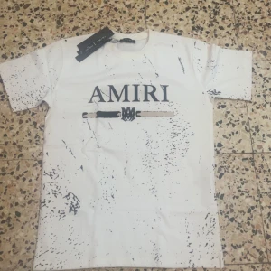 Helt ny vit Amiri t shirt  storlek L men passar också storlek M  - Snygg vit t-shirt från AMIRI i bomull med svart logotyptryck framtill och coolt stänkmönster över hela tröjan. Klassisk passform med rund hals och korta ärmar. Perfekt för dig som vill sticka ut med en streetinspirerad look.