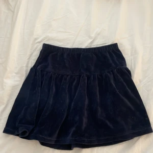 Mörkblå sammetskjol från H&M - Supersöt mörkblå kortkjol från H&M i mjuk sammet. Kjolen har en bred resår i midjan och ett lätt utställt fall med volang. Perfekt för dig som gillar en klassisk men ändå trendig look.