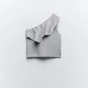 Grå oneshoulder topp med volang - GARDEROBSRENSNING! Snygg grå oneshoulder topp med stor volangdetalj över axeln. Använd 1 gång, passar perfekt för lite finare tillfällen!!