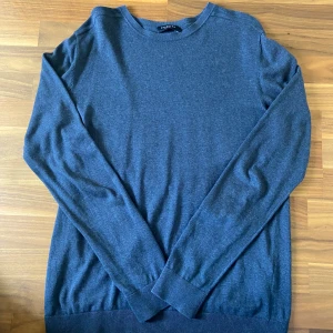 Mörkblå stickad tröja Selected Homme - En stilren mörkblå stickad tröja från Selected Homme. Tröjan har rund halsringning och långa ärmar, perfekt för lager-på-lager. Mjuk och skön känsla, passar till jeans eller chinos för en clean look.