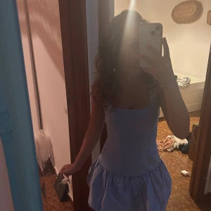 Ljusblå kort klänning med volangkjol - Supersöt ljusblå kort klänning med volangkjol. Klänningen har en figurnära överdel och en fluffig kjol som ger en lekfull vibe. Perfekt för varma dagar och somriga äventyr. Materialet känns lätt och bekvämt mot huden.