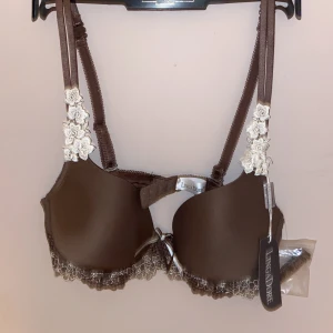 Brun bh med spets från LingaDore helt ny - Nypris 529kr          Supersnygg brun bh från LingaDore med dekorativa spetsdetaljer och blommiga broderier på axelbanden. Mjuk och följsam känsla tack vare materialmixen av polyester, nylon och elastan. Söt rosett framtill och extra band medföljer. 