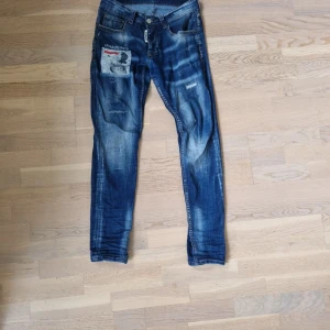 Blå skinny jeans med patch, strl 29 - Snygga blå skinny jeans från 2CON och Ibrahimovic i storlek 29. Jeansen har slitna detaljer, patch med tryck på vänster lår och klassisk femficksdesign. Materialet är bomull med lite stretch för skön passform. Perfekta för en cool och avslappnad look.