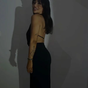 Svart långklänning med öppen rygg - Säljer en svart långklänning med djup v-ringning och öppen rygg. Klänningen har smala axelband och en tight passform som framhäver figuren. Perfekt för dig som vill sticka ut med en stilren och elegant look.