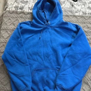 Blå hoodie från Bik Bok med huva - Enkel och snygg blå hoodie från Bik Bok i storlek S. Tröjan har huva med snörning, magficka och långa ärmar. Mindre fläck på framsidan, se bild.