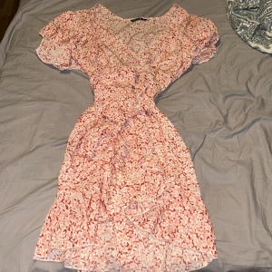 Blommig klänning från SHEIN - Supersöt kort klänning från SHEIN i röd och vit blommig design. Klänningen har volangdetaljer, knytband i midjan och korta ärmar. Perfekt för sommarens alla tillfällen och ger en fräsch och romantisk vibe.