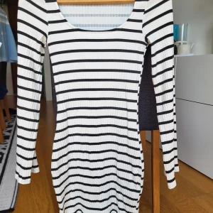 Randig ribbad klänning H&M Divided - Snygg ribbad kortklänning från H&M Divided i svart och vitt. Klänningen har lång ärm, rundad urringning och ett tight passform. De horisontella ränderna ger en cool och modern vibe, perfekt för dig som gillar enkel men trendig stil.