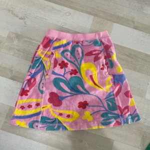 Färgglad blommig frotté-kjol - Superfin kortkjol i mjuk frotté med färgglatt blommönster i rosa, gult, blått, rött och grönt. Kjolen har bred resår i midjan och två fickor fram. Perfekt för sommarens alla äventyr och ger en riktigt glad vibe!