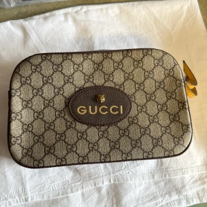 Gucci axelväska med GG-mönster - Säljer en snygg axelväska från Gucci i beige och brunt GG-monogram. Väskan har guldiga detaljer, avtagbar axelrem i grönt och rött samt dragkedja. Insidan är fodrad med blommigt tyg och har en innerficka med Gucci-logga.