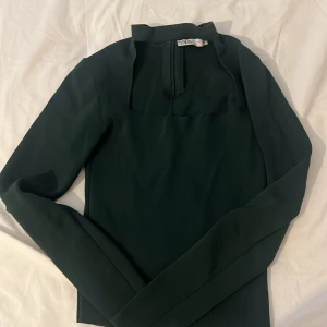Mörkgrön långärmad topp från Zara - Snygg mörkgrön långärmad topp från Zara med hög krage och dragkedja bak. Stilren och enkel design som passar perfekt till jeans eller kjol. Materialet känns mjukt och följsamt mot kroppen. Perfekt för dig som gillar minimalistisk stil.
