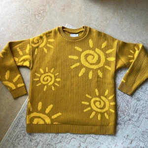 Gul stickad tröja med solmönster ASOS - Gul stickad tröja från ASOS DESIGN med solmönster i en ljusare gul nyans. Tröjan har ribbade muddar och rund hals, samt långärmad och oversized passform. Använd fåtal gånger och i fint skick