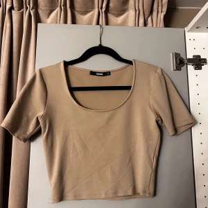 Beige croppad topp från Bik Bok - En stilren beige croppad topp från Bik Bok med korta ärmar och rund, djup urringning. Enkel och clean design som är lätt att matcha med olika outfits. Mjuk och stretchig bomullskänsla för en bekväm passform.