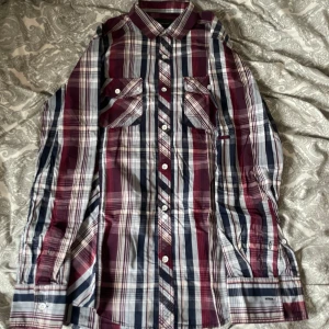 Rutig skjorta i rött och blått - Snygg rutig skjorta med långa ärmar i rött, blått och vitt. Skjortan har klassisk krage, knäppning framtill och två bröstfickor med knappar. Perfekt för en avslappnad och cool stil. Säljer mycket skjortor så köp gärna flera i ett bundle!