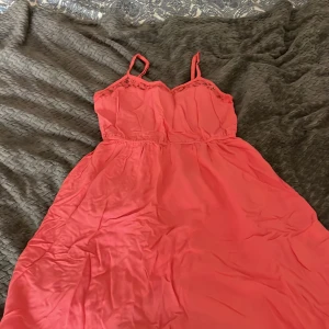 Korallrosa kortklänning från H&M Divided - Söt korallrosa kortklänning från H&M Divided med smala axelband och lätt rynkad midja. Klänningen har spetsdetaljer vid urringningen och är tillverkad i ett mjukt, tunt material som känns luftigt och skönt.