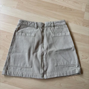 Beige kortkjol med dragkedja  - Fin beiga jeanskjol stl 34.  Används ca 3 gr. Kanske litelite urtvättad, inget man ser tydligt.