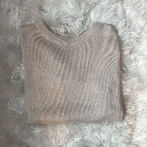 Beige stickad kortärmad tröja - Supermjuk och stilren beige stickad tröja med korta ärmar och rund hals. Tröjan har en ribbad struktur och är perfekt för lager-på-lager eller som den är. Enkel att matcha med både jeans och kjol.