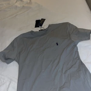 Grå t-shirt från Polo Ralph Lauren - Snygg grå t-shirt från Polo Ralph Lauren med klassisk passform och korta ärmar. Ikoniska lilla loggan broderad på bröstet. Perfekt basic-plagg i mjuk bomull som funkar till allt.