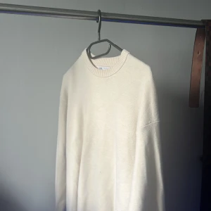Beige stickad tröja från Zara - En stilren beige stickad tröja från Zara med rund halsringning och ribbade muddar. Tröjan har en relaxed passform och långa ärmar, perfekt för lager-på-lager under kyliga dagar.