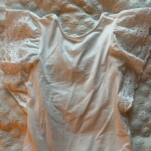 Vit body med broderade volangärmar Zara - Supersöt vit body från Zara med breda volangärmar i broderad bomull. Ärmarna har fina hålbroderier som ger en romantisk vibe. Perfekt för dig som gillar detaljer och vill ha en luftig topp med extra statement på ärmarna.