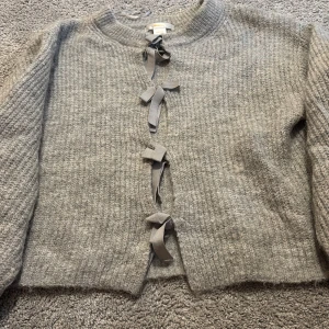 Grå stickad kofta med rosetter Gina Tricot - Supermysig grå stickad kofta från Gina Tricot med snygga rosett-detaljer framtill. Koftan har långärmade ärmar. 