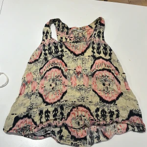 Mönstrad linnetopp från ONLY, strl 38 - Säljer en luftig linnetopp från ONLY med coolt grafiskt mönster i beige, svart och rosa. Toppen är ärmlös med breda axelband och har en avslappnad passform, perfekt för varma dagar. Materialet känns lätt och skönt mot huden.