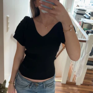 Svart v-ringad topp - Säljer en stilren svart topp med v-ringning och korta ärmar, har en v-ringning i back med en knyte. Perfekt för en enkel och elegant look. Passar bra till både jeans och kjol.